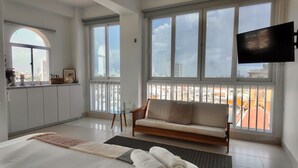 A modern living room with a sofa, a TV mounted on the wall, and large windows offering city views. - Apartment in the Historic Center with a great view- BARUC III (Cartagena de Indias)