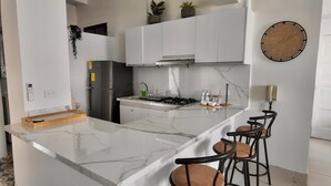 A modern kitchen with white cabinets, a marble countertop, a built-in stove, and a bar area with stools. - Apartment in the Historic Center with a great view- BARUC III (Cartagena de Indias)