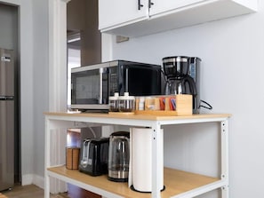 Cozinha equipada com micro-ondas, cafeteira e cápsulas de café numa prateleira.