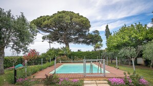 A swimming pool with a wooden deck, surrounded by a garden with various plants and flowers. - Podere Isabella - Mandarin apartment with large terrace overlooking the sea (Toscana)