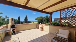 A covered patio with a brick floor, a grill, a chair, and a table. - Podere Isabella - Mandarin apartment with large terrace overlooking the sea (Toscana)