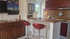 A modern kitchen with wooden cabinets, a stainless steel sink, and two red bar stools. - Podere Isabella - Mandarin apartment with large terrace overlooking the sea (Toscana)