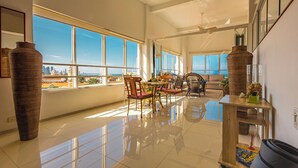 Amplia sala de estar con ventanas grandes, un comedor y vistas a un horizonte urbano.