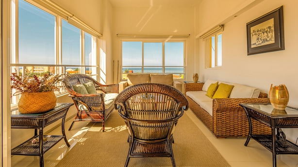 Amplia sala de estar con un gran ventanal con vista al océano, muebles de mimbre y un ventilador de techo.