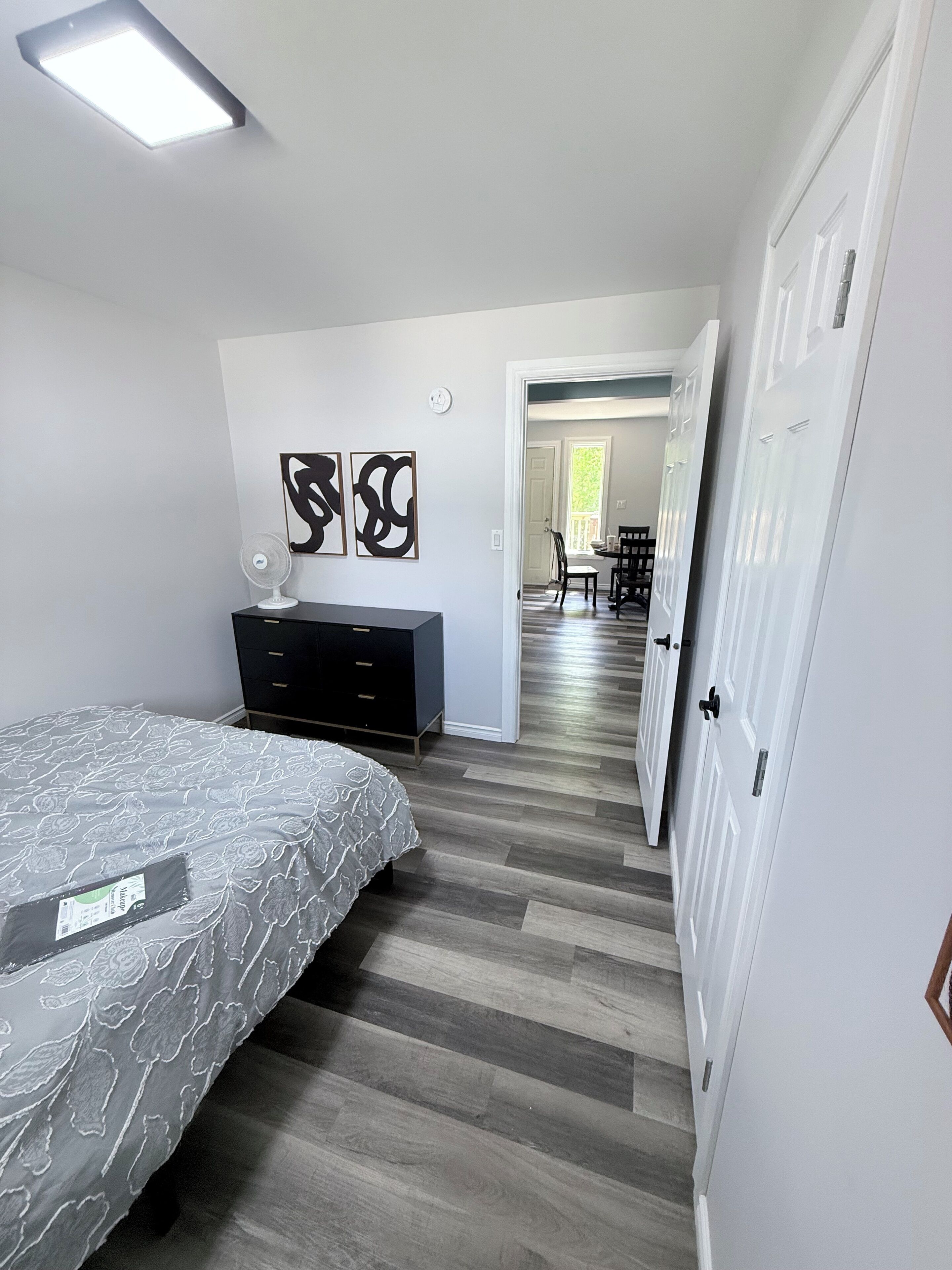 Une chambre à coucher comprenant un lit, une commode et deux tableaux abstraits accrochés au mur.
