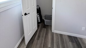 Une pièce avec une porte blanche, un placard où sont suspendus des vêtements, un panier à linge et un sac à linge.