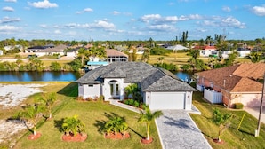 A residential house with a grey roof, white exterior walls, and a small front yard with palm trees.