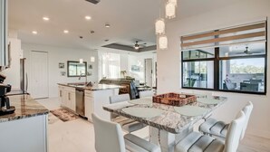 A modern kitchen with a marble countertop, white cabinetry, and a dining area with a marble table and white chairs.