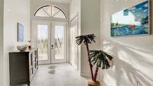 A hallway with a white door, a potted plant, and a painting on the wall.
