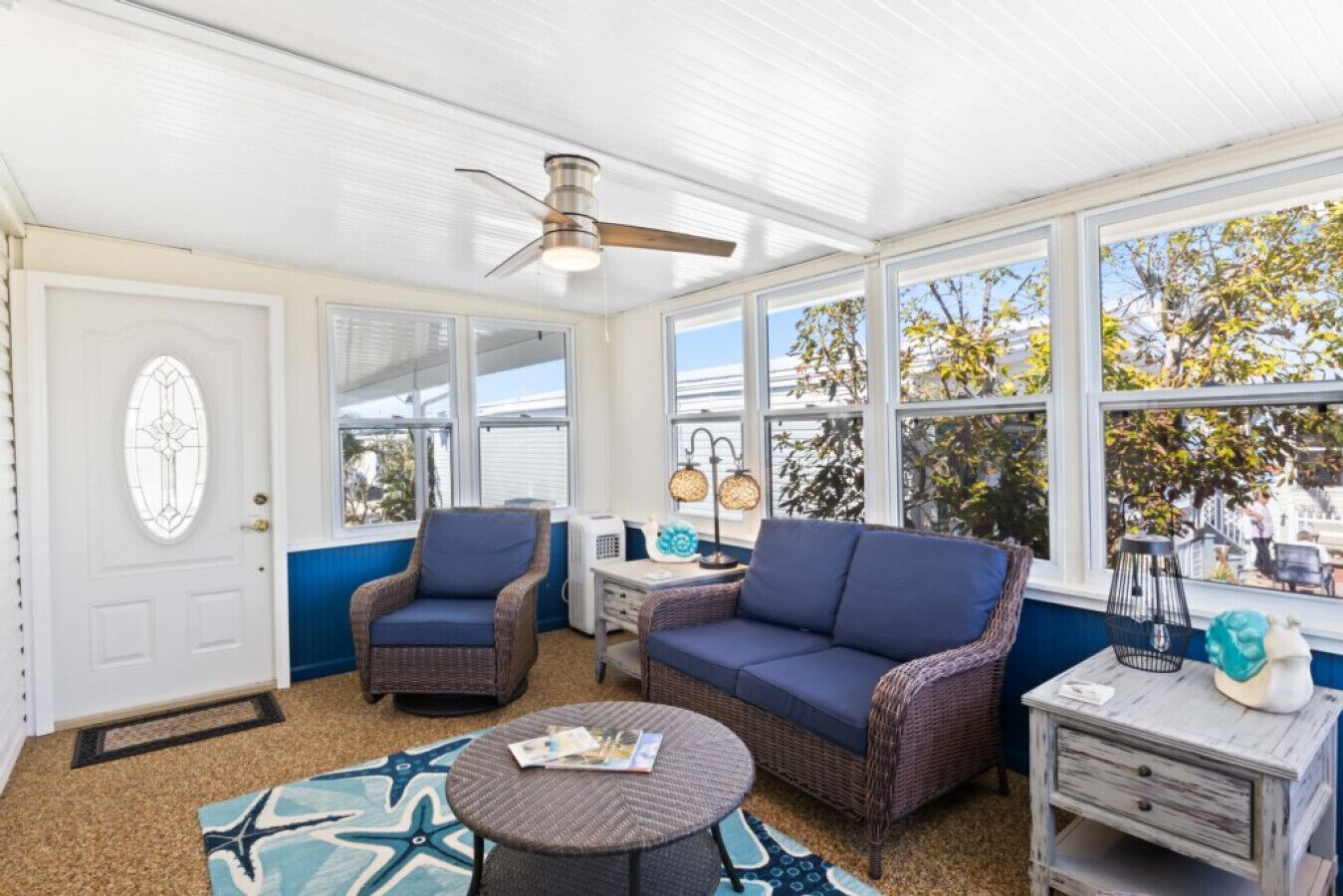 A sunroom with wicker furniture, a ceiling fan, and large windows offering views of the outdoors.