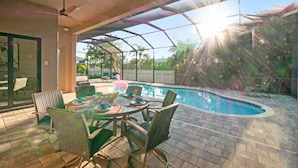An outdoor pool area with a glass enclosure, surrounded by wicker chairs and a dining table.