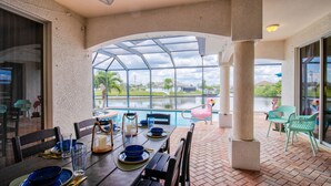 A covered outdoor dining area with a pool view, tables set with blue tableware, and chairs. - Beautiful Pool Home with Gulf access (Cape Coral)