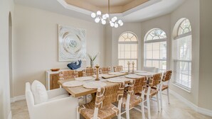 A dining room with a large wooden table, white chairs, and a chandelier. - Beautiful Pool Home with Gulf access (Cape Coral)