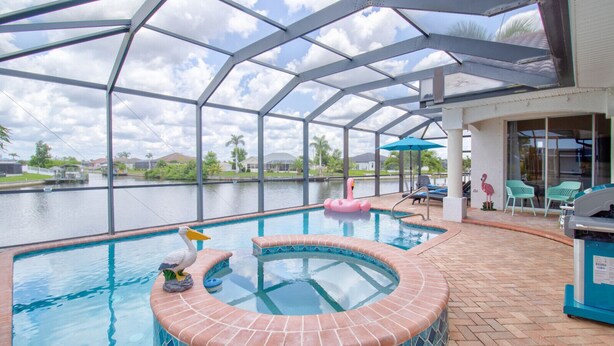 An indoor swimming pool with a glass ceiling, a hot tub, and a view of a water body outside. - Beautiful Pool Home with Gulf access (Cape Coral)