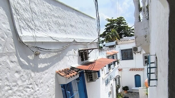 A narrow alleyway with white buildings, a blue gate, and a tiled roof. - Apartment in Colombian Santorini (Doradal)