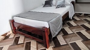 A bedroom with a bed, a wooden headboard, a geometric patterned floor, and a wall clock. - Apartment in Colombian Santorini (Doradal)