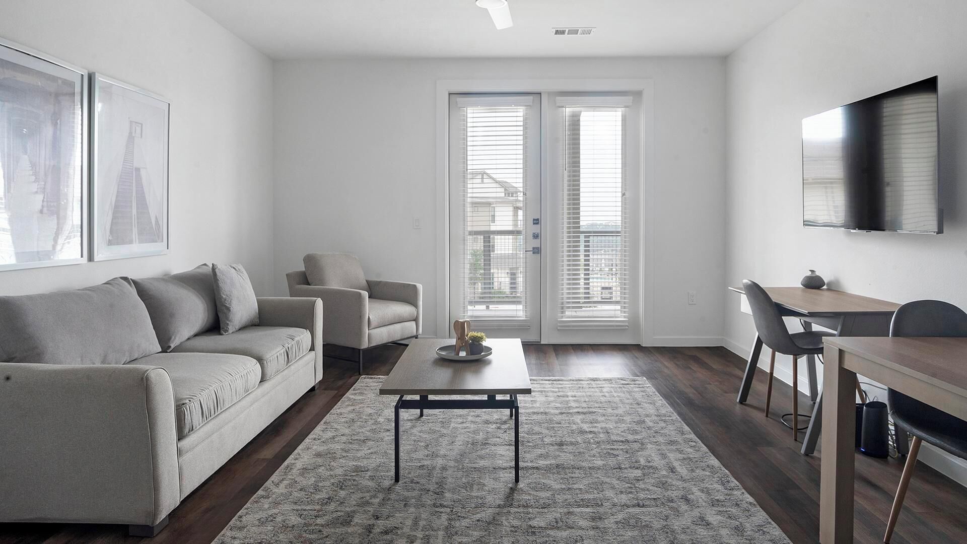 A modern living room with a grey sofa, a smaller armchair, a coffee table, and a dining area with a table and chairs.