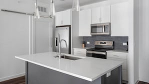 Une cuisine moderne avec des meubles blancs, des appareils en acier inoxydable et des luminaires suspendus.