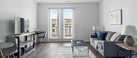 A modern living room with a flat-screen TV, a sofa, a coffee table, and a dining area with a table and chairs.