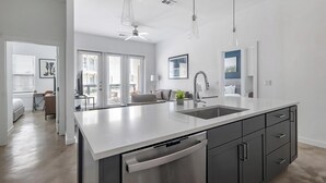 Een moderne keuken met een groot eiland, roestvrijstalen apparatuur en uitzicht op de woonkamer.