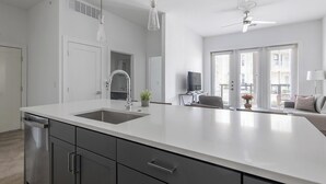 Een moderne keuken met een groot eiland, inbouwapparatuur en een zithoek met een bank en televisie.