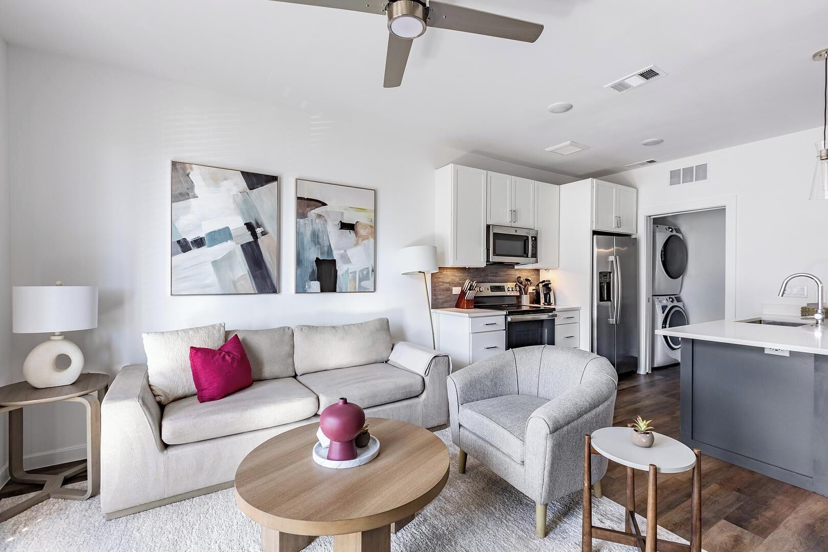 A modern living room with a sofa, armchair, coffee table, and artwork on the wall.