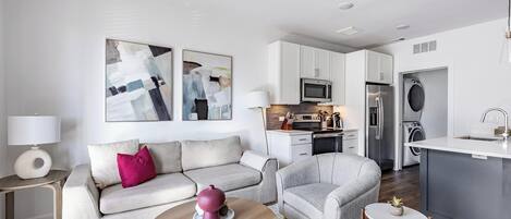 A modern living room with a sofa, armchair, coffee table, and artwork on the wall.