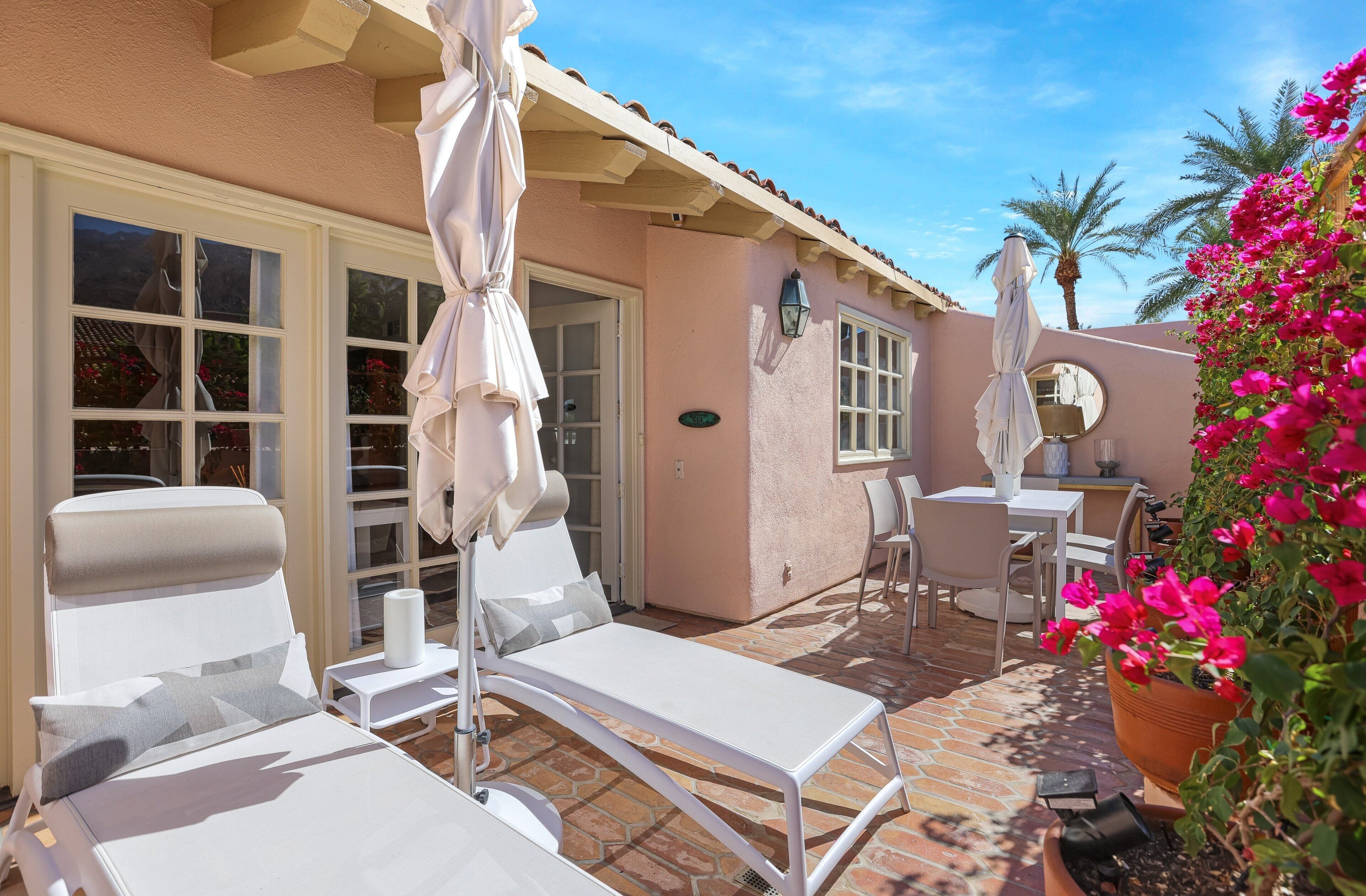 A patio area with white lounge chairs, a table, and a potted plant with pink flowers.