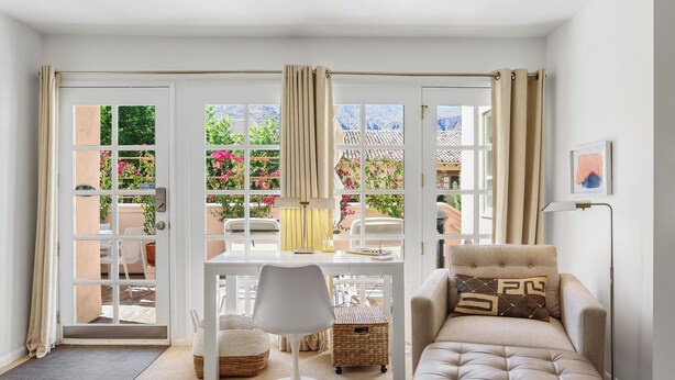 A living room with a sofa, a chair, a small table, and a view of a garden through large windows. - Keith Haring Inspired 2BD Deauville (Palm Springs)