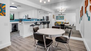 A modern kitchen with white cabinets, stainless steel appliances, and a central island. There is a dining area with a round table and chairs. - Quaint & Serene in Mesquite CC (Palm Springs)