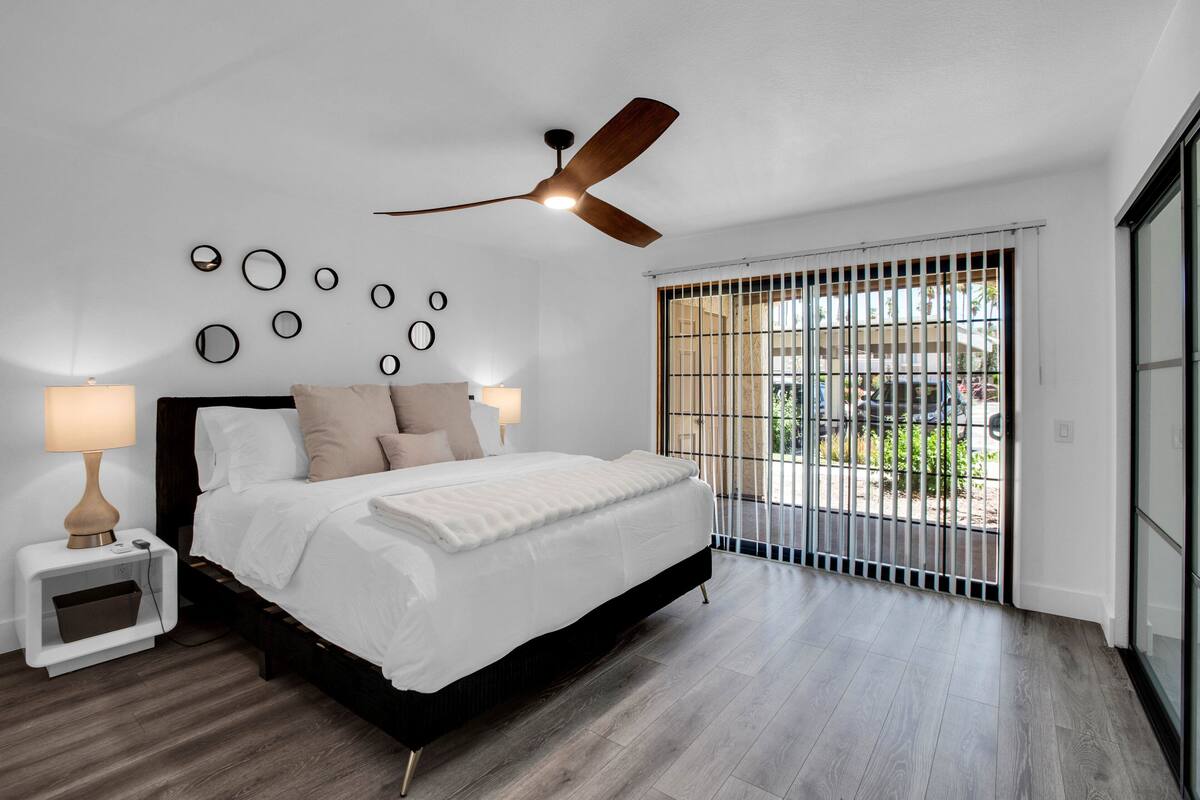A modern bedroom with a large bed, a ceiling fan, and a view through a barred window.