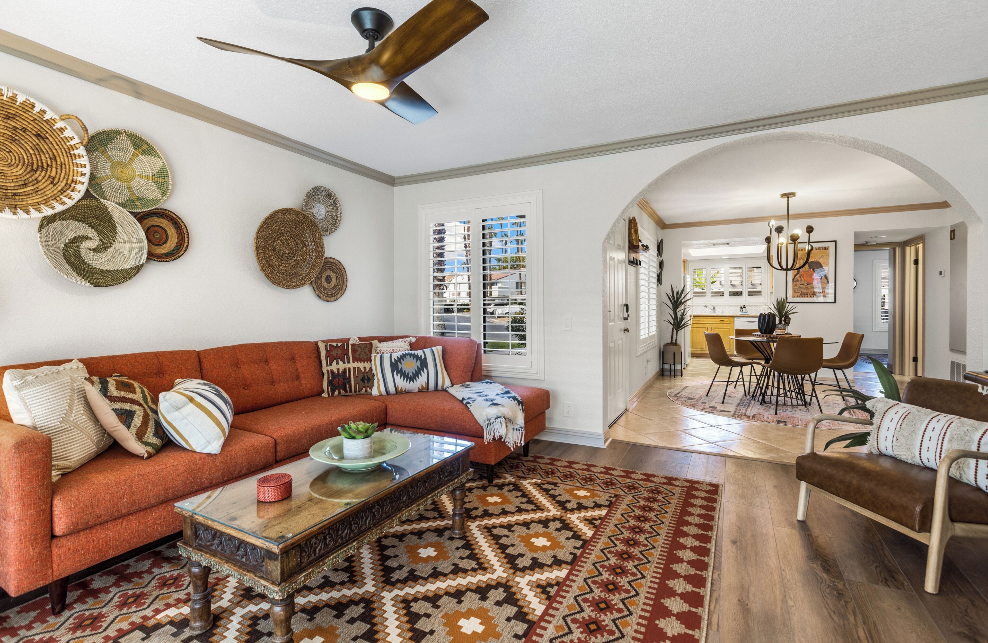 A spacious living room with a large sofa, coffee table, and decorative rugs. A dining area with chairs and a table is visible in the background.