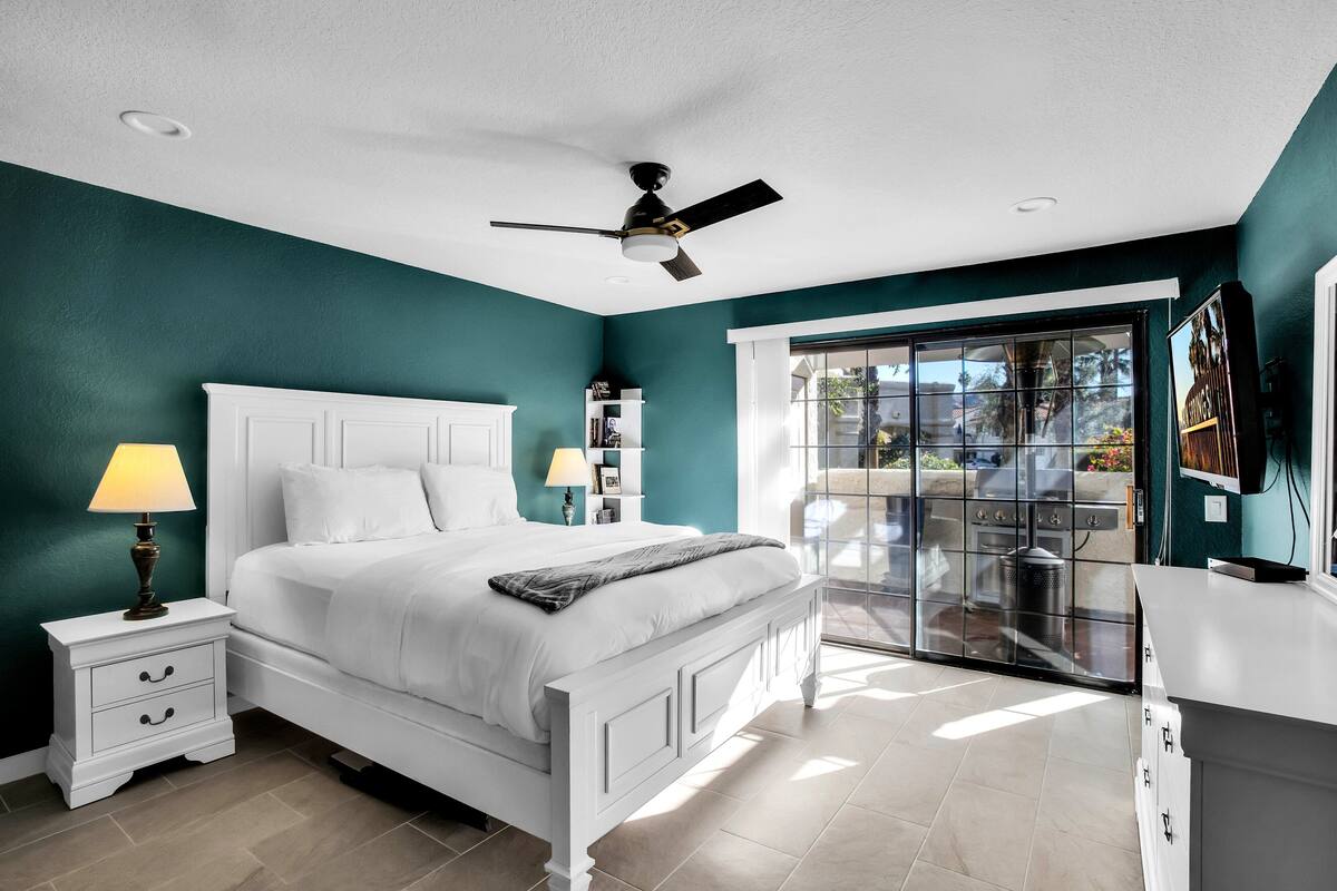 A bedroom with a bed, nightstands, a ceiling fan, and a view through a glass door to an outdoor area.