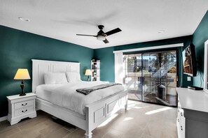 A bedroom with a bed, nightstands, a ceiling fan, and a view through a glass door to an outdoor area.