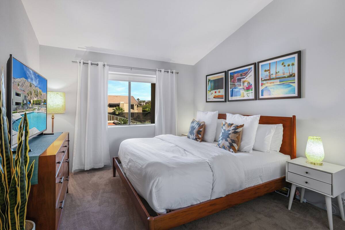 Habitación de hotel con una cama grande, televisión, mesita de noche y ventana con cortinas.