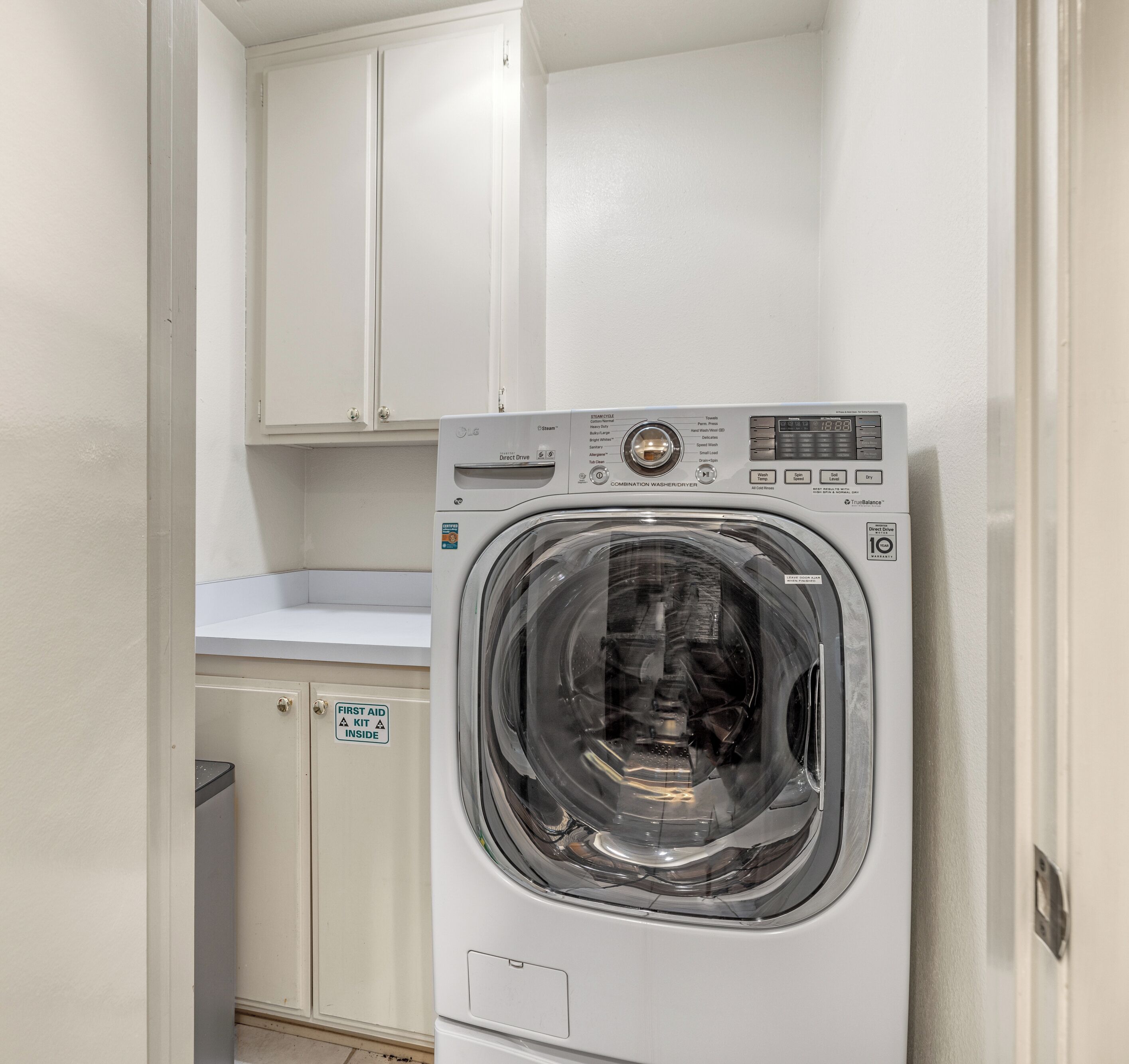 A compact washer and dryer unit with a control panel, a transparent door, and a "First Aid Kit Inside" sign.