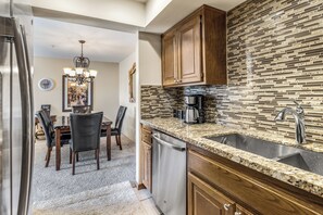 A kitchen with a granite countertop, stainless steel sink, and wooden cabinets. - Gated Urban Palm Escape (Palm Springs)
