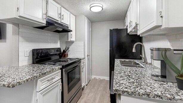 Una cocina compacta con armarios blancos, un refrigerador negro, un lavamanos de acero inoxidable y encimeras de granito.