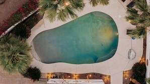 Luftaufnahme eines Schwimmbeckens, umgeben von Palmen und einer Pflasterterrasse.
