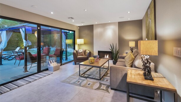 A modern living room with a glass door leading to an outdoor seating area, a fireplace, and a coffee table with decorative items. - Casa San Marino (Palm Springs)