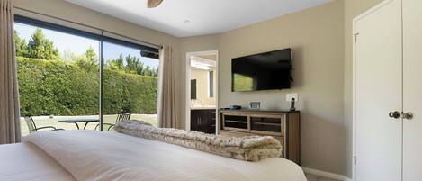 A bedroom with a large bed, a ceiling fan, a TV mounted on the wall, and a sliding glass door leading to an outdoor area.
