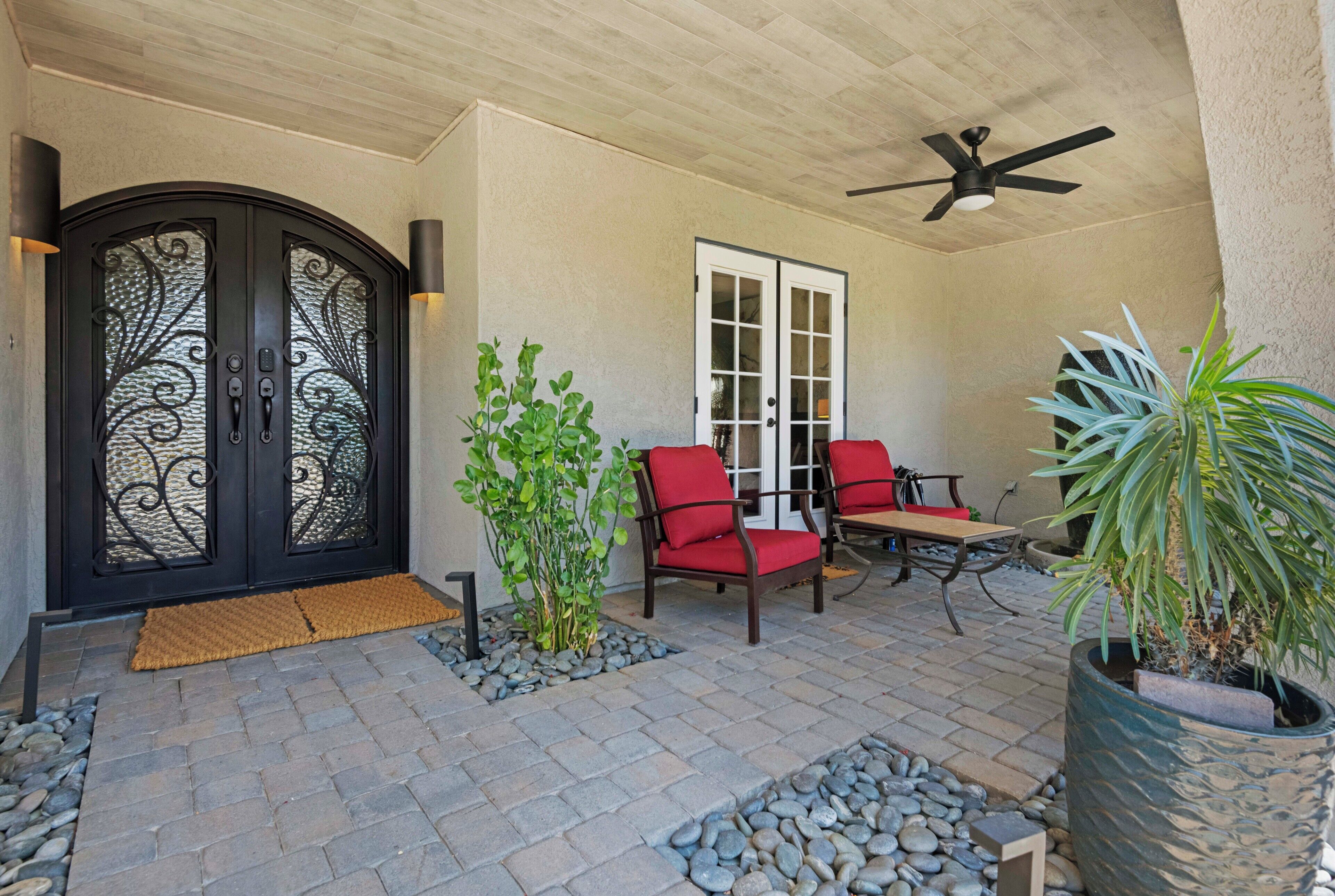 An outdoor patio with a black gate, red chairs, a ceiling fan, and potted plants.