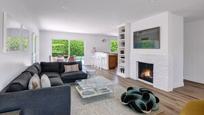 Ein modernes Wohnzimmer mit Kamin, Sofa, Couchtisch und Blick auf Pool und Außenbereich.