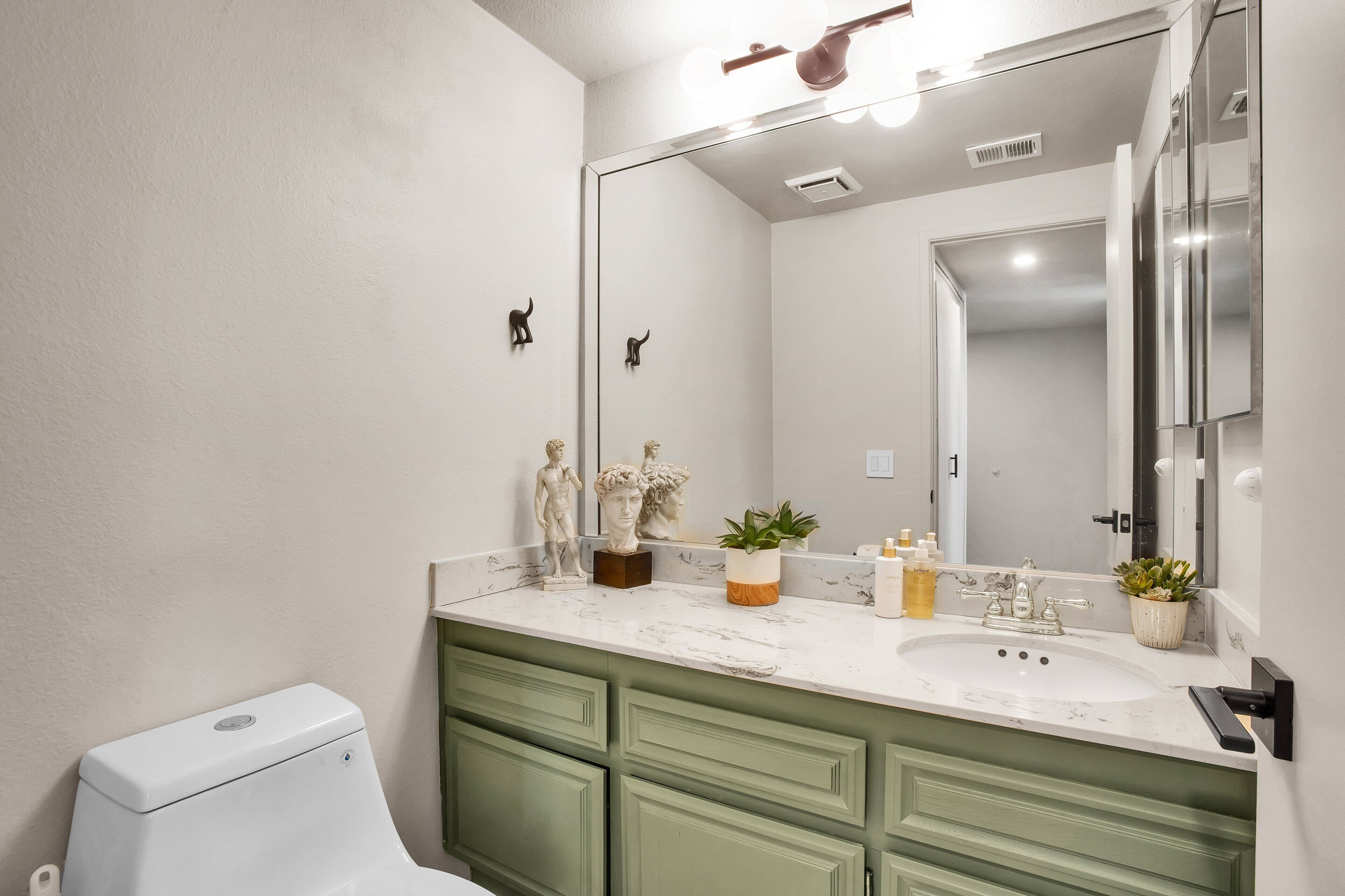 A bathroom with a white toilet, green cabinets, a marble sink, and a large mirror.