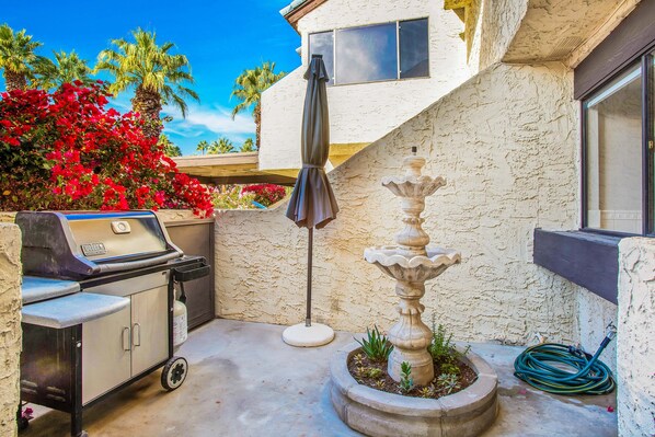 Un patio con una parrilla, una fuente de piedra y un paraguas grande.