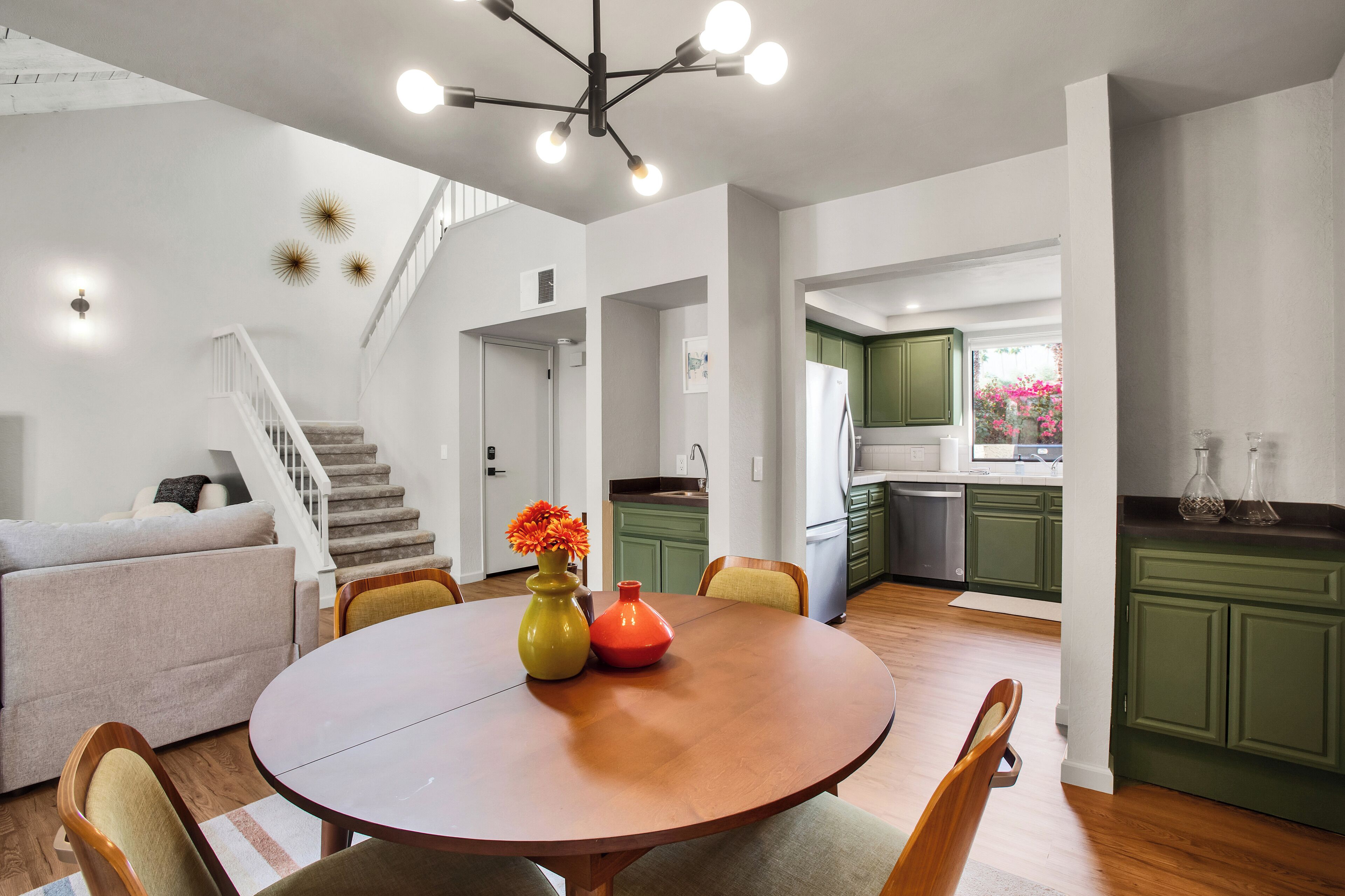 A modern kitchen with green cabinets, a dining area with a wooden table, and a staircase leading to another level.