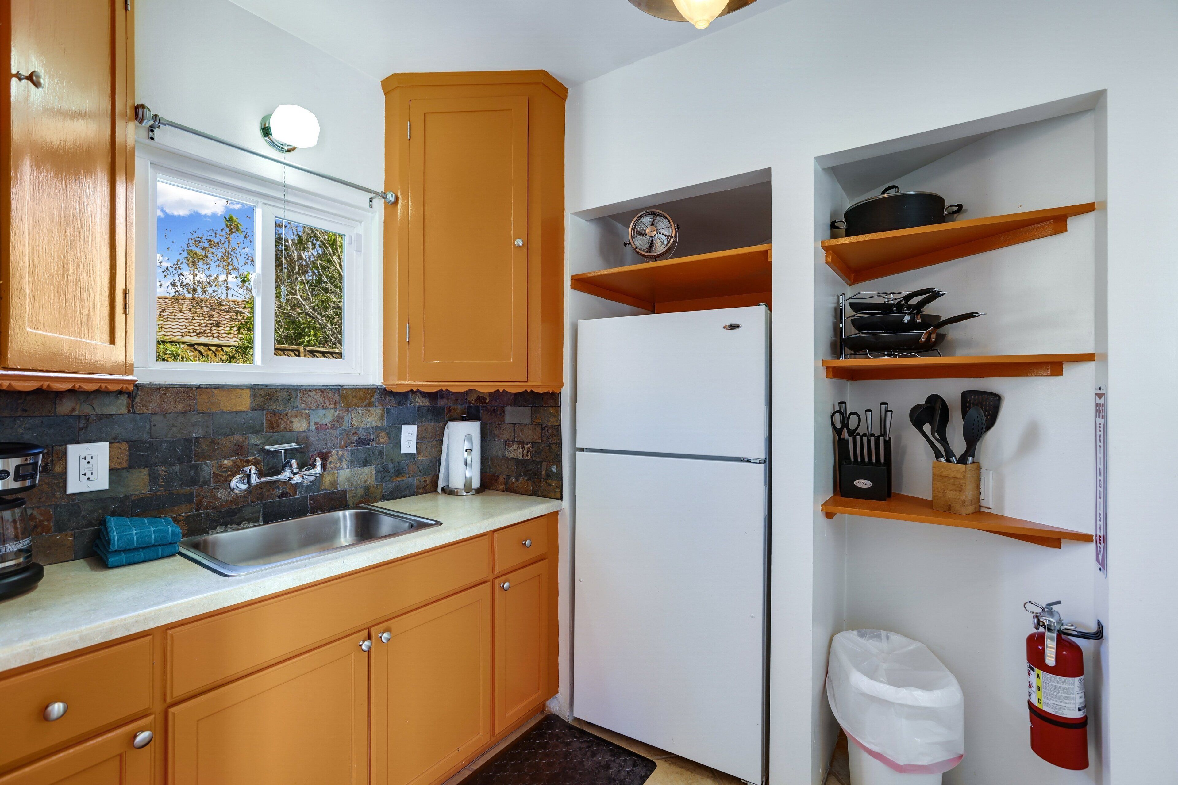 A kitchen with wooden cabinets, a stainless steel sink, a white refrigerator, and a window with a view of trees.
