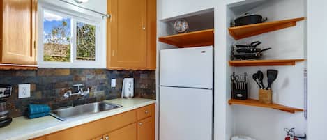 A kitchen with wooden cabinets, a stainless steel sink, a white refrigerator, and a window with a view of trees.