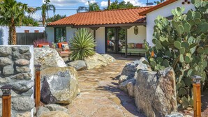 Une maison avec un toit recouvert de tuiles rouges, un chemin de pierres et de grands cactus.
