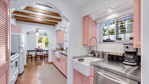 Une cuisine avec des meubles de rangement roses, une machine à café et une fenêtre avec des stores.